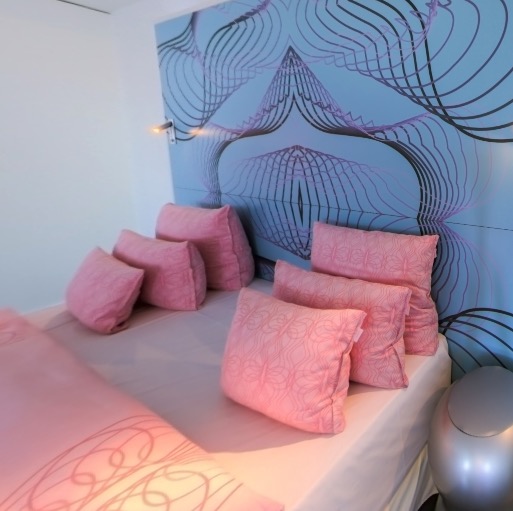 Bed with pink cushions against psychedelic wallpaper